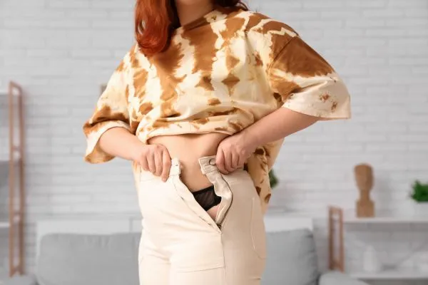 Image of woman trying to do her trousers up after pregnancy weight gain Berkhamsted