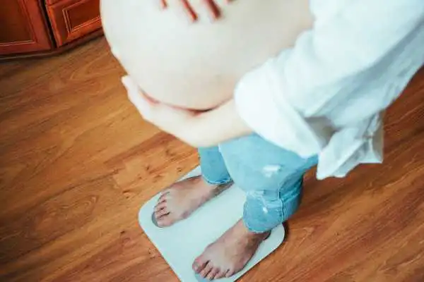 Image of woman weighing herself and experiencing weight gain through pregnancy Berkhamsted
